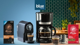 Koffiezetapparaat en koffiecups van Perla samen met filterkoffie en koffiemachine, gepresenteerd op een keukenachtergrond met blauwe tegelwand.