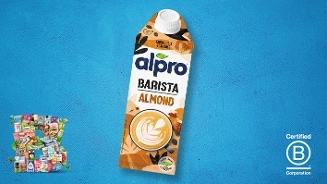 Alpro Barista Amandeldrink in een kartonnen pak op een blauwe achtergrond, met latte art op de verpakking, een collage van producten linksonder en het Certified B Corporation logo rechtsonder.