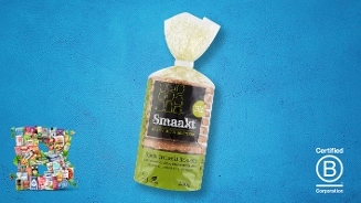Biologisch spelt muesli koeken van het merk Smaakt in een plastic verpakking op een blauwe achtergrond, met het B Corporation keurmerk en een collage van biologische producten links onderin.