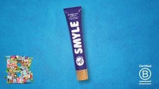 Paarse tube SMYLE tandpasta met houten dop op een blauwe achtergrond, links onderin een collage van diverse producten en rechtsonder het Certified B Corporation logo.