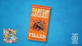 Tony's Chocolonely FIlled melk karamel zeezout chocoladereep op een blauwe achtergrond, met een collage van andere producten linksonder en het Certified B Corporation logo rechtsonder.