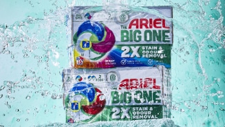 Verpakking van Ariel The Big One wasmiddel met 2x vlek- en geurverwijdering, gedecoreerd met kleurrijke waterdruppels.