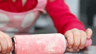 Kind rolt deeg uit met een roze deegroller.
