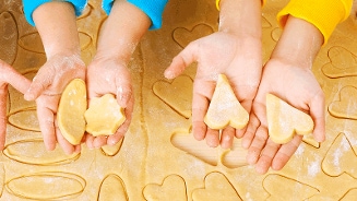 Kinderen maken koekjes met verschillende uitsteekvormpjes op een deegvel.