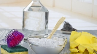 Schoonmaakproducten met fles witte azijn, kom met poeder, spons, borstel en gele rubberen handschoenen op een tafel.