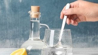 Glas water met een hand die roert, naast een karaf en halve citroen.