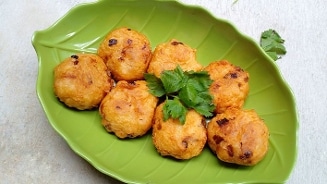 Balletjes van gefrituurd deeg met stukjes ui, geserveerd op een groen bladvormig bord met koriandergarnering