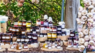 Potjes jam en chutney uitgestald op een marktstand, omringd door strengen knoflook