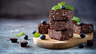 Stapel chocolade brownies met stukjes noot, gegarneerd met blauwe bessen en verse munt op een houten plank