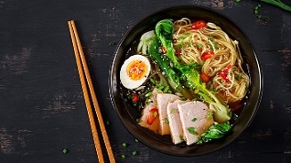 Kom met Japanse ramen noedelsoep, geserveerd met plakjes varkensvlees, gekookt ei, paksoi, rode peper en verse groenten, met houten eetstokjes ernaast op een donkere ondergrond