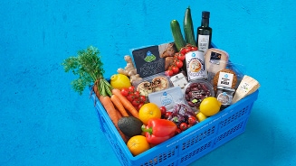 Blauwe boodschappenkrat gevuld met diverse verse groenten, fruit, kruiden, kaas en andere levensmiddelen van Albert Heijn, op een blauwe achtergrond.