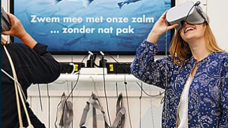 Mensen gebruiken VR-headsets voor een viservaring met de tekst "Zwem mee met onze zalm ... zonder nat pak" op het scherm.