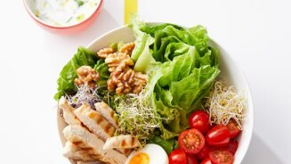 Salade met gegrilde kip, walnoten, gekookte eieren, tomaten en sla, geserveerd met een kom yoghurt-dressing.
