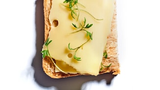 Een sneetje brood belegd met een plakje kaas en verse kruiden.