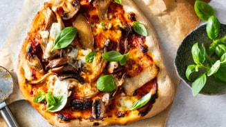 Huisgemaakte pizza met champignons en verse basilicum op bakpapier, naast een pizzasnijder.