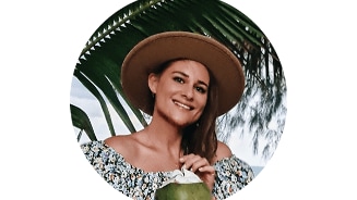 Profielfoto van Rebecca met een hoed, een groene kokosnoot en een achtergrond van palmbomen.