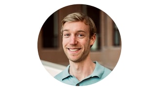 Portret van een man met een wazig gezicht, gekleed in een lichtblauw poloshirt, met een bakstenen gebouw op de achtergrond.