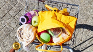 Fietsmand met picknickspullen, inclusief een gele tas, groene appel, handdoek en drinkflessen.
