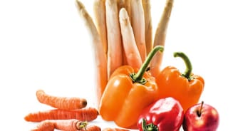 Witte asperges, oranje paprika's, rode paprika en wortels met een rode appel op een witte achtergrond.