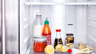 Koelkast gevuld met diverse producten zoals melk, saus, kikkomansojasaus, citroen en smeerbare boter.
