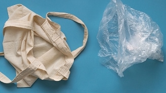 Herbruikbare katoenen tas naast een plastic tas op een blauwe achtergrond.