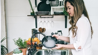 Vrouw wast een bord in een moderne keuken met planten en fruit op het aanrecht.