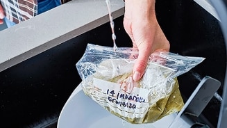 Plastic zakje met zelfgemaakte soep onder stromend water in de keuken, met datumlabel.