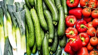 Prei, komkommers, rode paprika's en tomaten naast elkaar op een oppervlak.