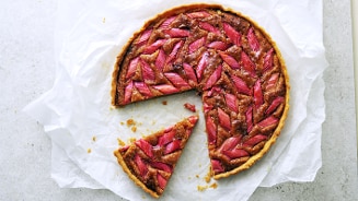 Rabarbertaart met een stuk eruit gesneden, op bakpapier gelegd.