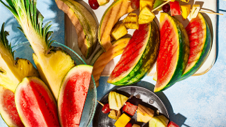 Schijven watermeloen, stukken ananas, banaan en kleurrijke fruitspiezen met druiven, meloen en ananas op een zomerse ondergrond.