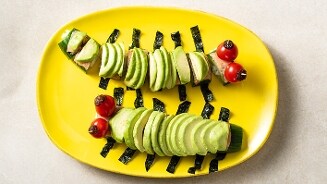 Kindertraktatie gemaakt van toast en avocado in de vorm van een rups op een geel bord voor het afscheid op het kinderdagverblijf