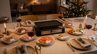 Gezellige kersttafel gedekt met gourmetstel, diverse schalen met vlees, vis en groenten, wijnglazen en decoratieve kerstaccessoires, met een versierde kerstboom op de achtergrond.