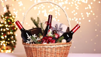 Feestelijk gevulde geschenkenmand met drie flessen rode wijn, cadeauverpakkingen en kerstdecoraties op een lichte achtergrond met sfeerverlichting