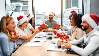 Collega’s met kerstmutsen wisselen cadeaus uit tijdens een kerstviering op kantoor