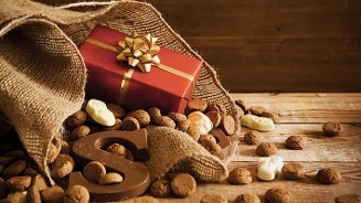 Sinterklaas lekkernijen op houten tafel met jute zak, chocoladeletter S, pepernoten, schuimpjes en een rood cadeautje met gouden strik