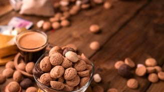 Kruidnoten in een glazen schaal met een kopje koffie op een houten tafel