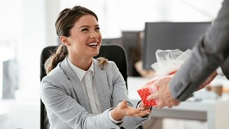 Vrouw in kantoor ontvangt een ingepakt cadeau van een collega