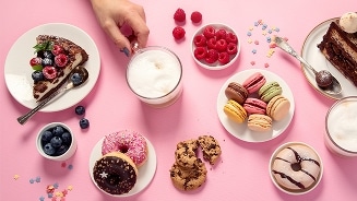 Assortiment van kleurrijke macarons, donuts, taartpunten met bessen, verse frambozen, blauwe bessen, chocoladekoekjes en cappuccino op een roze ondergrond