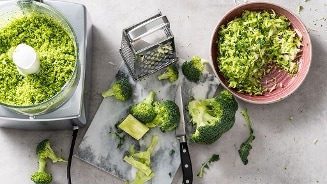 Bereiding van broccoli rijst met keukenmachine en rasp op een keukenaanrecht.