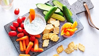 Gezond borrelplankje met komkommers, cherrytomaatjes, wortels, paprikareepjes, crackers en een dip.
