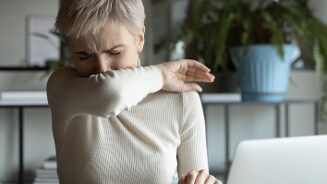 Persoon nyest in elleboog in een binnenruimte met planten op de achtergrond.