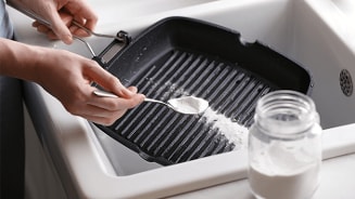 Een gietijzeren grillpan wordt schoongemaakt met zuiveringszout in een gootsteen.
