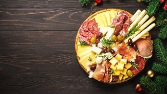 Borrelplank met diverse soorten kaas, vleeswaren, olijven en grissini op een houten ondergrond, feestelijk gedecoreerd met kerstgroen en kerstballen