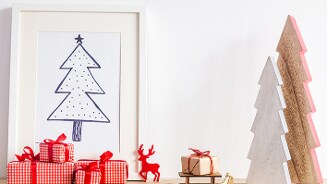 Kerstdecoratie met cadeautjes en een getekende kerstboom in een lijst.