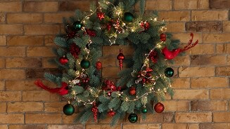 Kerstkrans met decoraties en verlichting aan een bakstenen muur