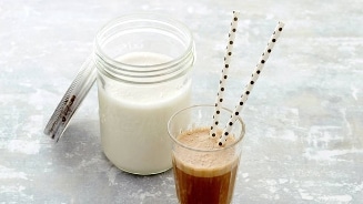 Zelfgemaakte amandelmelk naast een glas met een drankje en papieren rietjes.