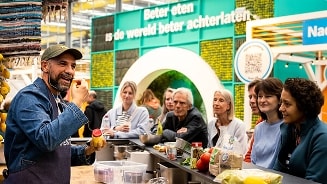 Kookdemonstratie bij Albert Heijn met de slogan "Beter eten is de wereld beter achterlaten" op de achtergrond.