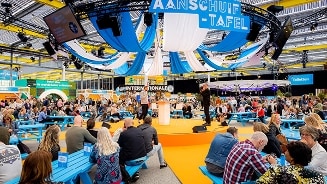 Beter eten aanschuiftafel evenement van Albert Heijn met mensen zittend aan blauwe tafels.
