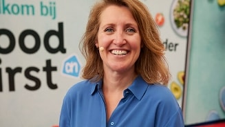 Portret van een vrouw in blauwe blouse, met een achtergrond die verwijst naar Albert Heijn's "Food First" campagne.