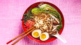 Kleurrijke kom ramen met eieren, shiitake-paddenstoelen, zeewier, paksoi en noedels, op een roze achtergrond.
